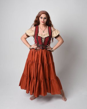 Ortaçağ bakiresi, falcı kostümü giymiş güzel kızıl saçlı bir kadının tam boy portresi. Dans hareketleriyle ayakta durmak, etek sallamak. Stüdyo arka planında izole.
