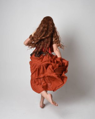 Ortaçağ bakiresi, falcı kostümü giymiş güzel kızıl saçlı bir kadının tam boy portresi. Geri görüş pozisyonunu alıyor, uzaklaşıyor. Stüdyo arka planında izole.