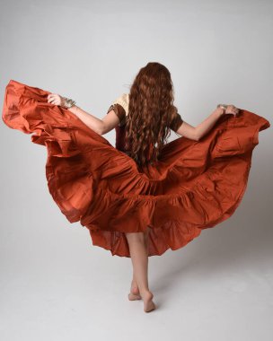 Ortaçağ bakiresi, falcı kostümü giymiş güzel kızıl saçlı bir kadının tam boy portresi. Geri görüş pozisyonunu alıyor, uzaklaşıyor. Stüdyo arka planında izole.