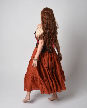 Full length portrait of beautiful red haired woman wearing a medieval maiden, fortune teller costume. Standing pose back view, walking away. isolated on studio background. clipart