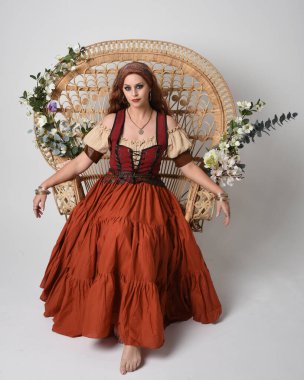 Full length portrait of beautiful red haired woman wearing a medieval maiden, fortune teller costume.  Sitting pose, with gestural hands reaching out. isolated on studio background. clipart