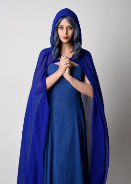 Close up portrait of beautiful female model wearing elegant fantasy blue ball gown, flowing cape with hooded cloak.Gestural arms reaching out. Isolated on white studio background. clipart