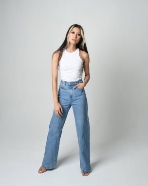 Esmer kadın Asyalı modelin günlük giysiler, beyaz atlet gömlek ve kot pantolon giymiş tam boy portresi. Kameraya dönük poz. Beyaz stüdyo arka planında izole edilmiş..
