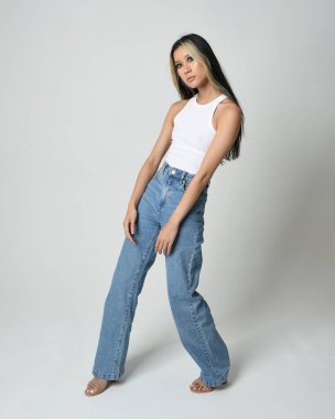 Esmer kadın Asyalı modelin günlük giysiler, beyaz atlet gömlek ve kot pantolon giymiş tam boy portresi. Kameraya dönük poz. Beyaz stüdyo arka planında izole edilmiş..