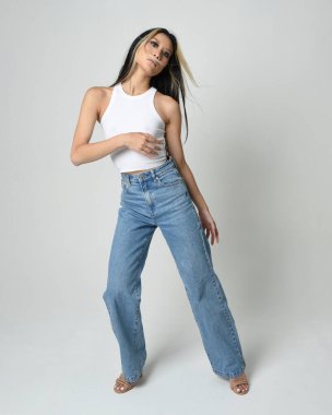 Esmer kadın Asyalı modelin günlük giysiler, beyaz atlet gömlek ve kot pantolon giymiş tam boy portresi. Kameraya dönük poz. Beyaz stüdyo arka planında izole edilmiş..