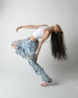 Esmer kadın Asyalı modelin günlük giysiler, beyaz atlet gömlek ve kot pantolon giymiş tam boy portresi. Enerjik zıplama, dans pozisyonu. Beyaz stüdyo arka planında izole edilmiş..