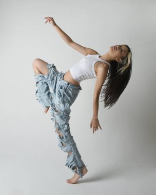 Esmer kadın Asyalı modelin günlük giysiler, beyaz atlet gömlek ve kot pantolon giymiş tam boy portresi. Enerjik zıplama, dans pozisyonu. Beyaz stüdyo arka planında izole edilmiş..