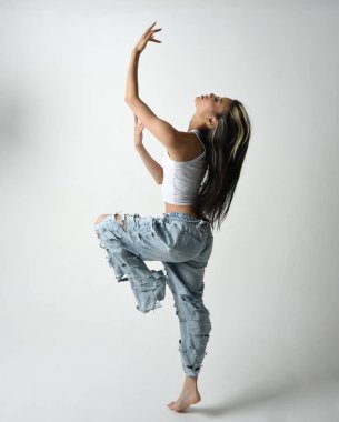 Esmer kadın Asyalı modelin günlük giysiler, beyaz atlet gömlek ve kot pantolon giymiş tam boy portresi. Enerjik zıplama, dans pozisyonu. Beyaz stüdyo arka planında izole edilmiş..