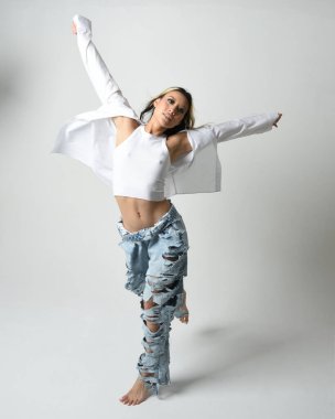Esmer kadın Asyalı modelin günlük giysiler, beyaz atlet gömlek ve kot pantolon giymiş tam boy portresi. Enerjik zıplama, dans pozisyonu. Beyaz stüdyo arka planında izole edilmiş..