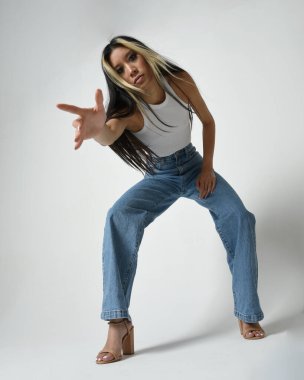 Esmer kadın Asyalı modelin günlük giysiler, beyaz atlet gömlek ve kot pantolon giymiş tam boy portresi. Rahat bir poz. Beyaz stüdyo arka planında izole edilmiş..