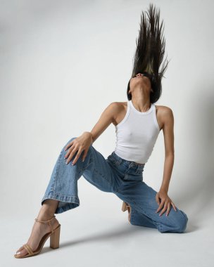 Esmer kadın Asyalı modelin günlük giysiler, beyaz atlet gömlek ve kot pantolon giymiş tam boy portresi. Rahat bir poz. Beyaz stüdyo arka planında izole edilmiş..