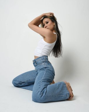 Esmer kadın Asyalı modelin günlük giysiler, beyaz atlet gömlek ve kot pantolon giymiş tam boy portresi. Rahat bir poz. Stüdyo arka planında izole edilmiş.