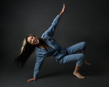 Esmer kadın Asyalı modelin günlük giysiler ve çift kot pantolon giymiş tam boy portresi. Karanlık stüdyo arka planında gölgelerle izole edilmiş.