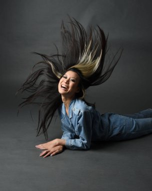 Esmer kadın Asyalı modelin günlük giysiler ve çift kot pantolon giymiş tam boy portresi. Karanlık stüdyo arka planında gölgelerle izole edilmiş.