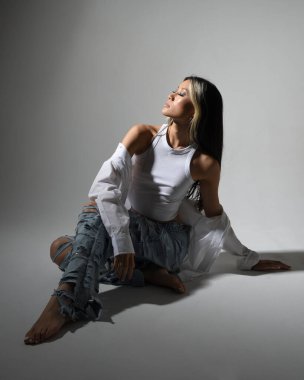 Esmer kadın Asyalı modelin günlük giysiler ve çift kot pantolon giymiş tam boy portresi. Karanlık stüdyo arka planında gölgelerle izole edilmiş.