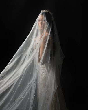 Beyaz gelinlik giymiş güzel bir mankenin yakın portresi ve kefen gibi akan bir duvak. Huysuz sinematik ışıklandırma, karanlık bir stüdyonun arka planında izole edilmiş..