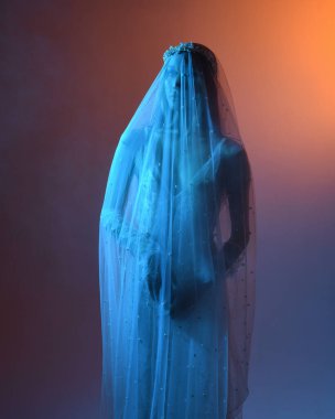 Beyaz gelinlik giymiş güzel bir mankenin yakın portresi ve kefen gibi akan bir duvak. Huysuz sinematik ışıklandırma, karanlık bir stüdyonun arka planında izole edilmiş..