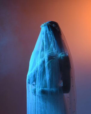 Beyaz gelinlik giymiş güzel bir mankenin yakın portresi ve kefen gibi akan bir duvak. Huysuz sinematik ışıklandırma, karanlık bir stüdyonun arka planında izole edilmiş..