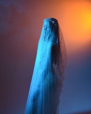 Beyaz gelinlik giymiş güzel bir mankenin yakın portresi ve kefen gibi akan bir duvak. Huysuz sinematik ışıklandırma, karanlık bir stüdyonun arka planında izole edilmiş..