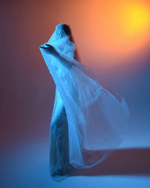 Beyaz gelinlik giymiş güzel bir mankenin yakın portresi ve kefen gibi akan bir duvak. Huysuz sinematik ışıklandırma, karanlık bir stüdyonun arka planında izole edilmiş..