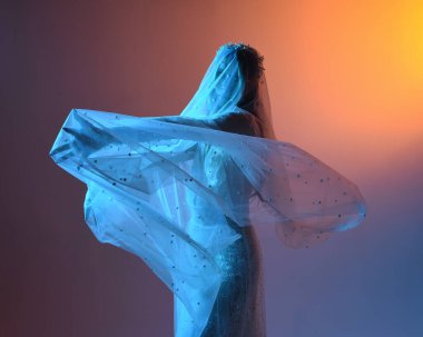 Beyaz gelinlik giymiş güzel bir mankenin yakın portresi ve kefen gibi akan bir duvak. Huysuz sinematik ışıklandırma, karanlık bir stüdyonun arka planında izole edilmiş..