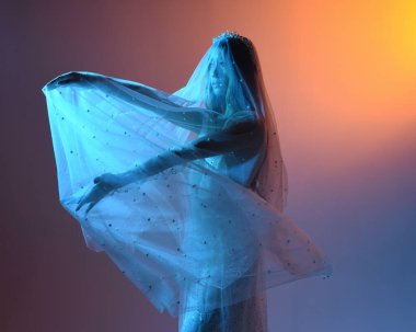 Beyaz gelinlik giymiş güzel bir mankenin yakın portresi ve kefen gibi akan bir duvak. Huysuz sinematik ışıklandırma, karanlık bir stüdyonun arka planında izole edilmiş..