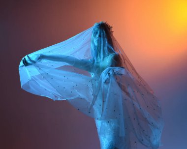 Beyaz gelinlik giymiş güzel bir mankenin yakın portresi ve kefen gibi akan bir duvak. Huysuz sinematik ışıklandırma, karanlık bir stüdyonun arka planında izole edilmiş..