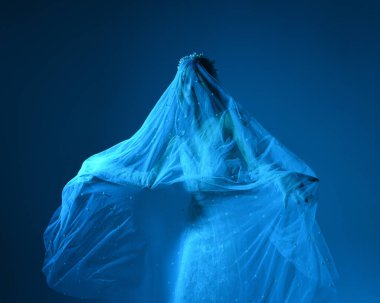 Beyaz gelinlik giymiş güzel bir mankenin yakın portresi ve kefen gibi akan bir duvak. Huysuz sinematik ışıklandırma, karanlık bir stüdyonun arka planında izole edilmiş..