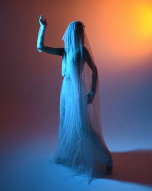 Beyaz gelinlik giymiş güzel bir mankenin yakın portresi ve kefen gibi akan bir duvak. Huysuz sinematik ışıklandırma, karanlık bir stüdyonun arka planında izole edilmiş..