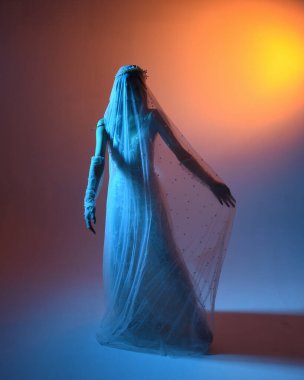 Beyaz gelinlik giymiş güzel bir mankenin yakın portresi ve kefen gibi akan bir duvak. Huysuz sinematik ışıklandırma, karanlık bir stüdyonun arka planında izole edilmiş..