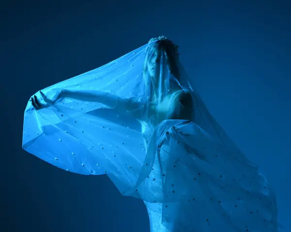 stock image Close up portrait of beautiful model wearing white wedding gown and ghostly flowing veil like a shroud. Moody cinematic lighting, isolated on a dark studio background.