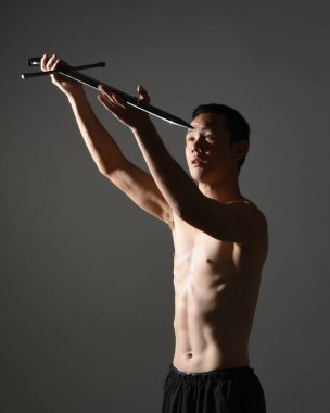 Yakışıklı Asyalı erkek modelin portresi, spor şortu ve üstsüz. Savaşçı eğitimleri sırasında kılıçlarını tutarken kasvetli karanlık stüdyo arka planında siluet ile izole edilmiş pozlar veriyordu.