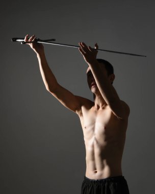 Yakışıklı Asyalı erkek modelin portresi, spor şortu ve üstsüz. Savaşçı eğitimleri sırasında kılıçlarını tutarken kasvetli karanlık stüdyo arka planında siluet ile izole edilmiş pozlar veriyordu.