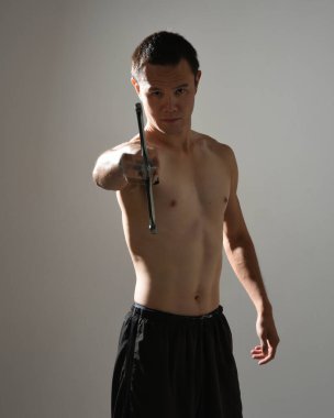 Yakışıklı Asyalı erkek modelin portresi, spor şortu ve üstsüz. Savaşçı eğitimleri sırasında kılıçlarını tutarken kasvetli karanlık stüdyo arka planında siluet ile izole edilmiş pozlar veriyordu.