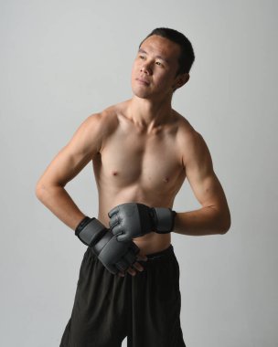 Formda Asyalı erkek modelin yakın portresi, kaslı üstsüz. Spor stenografisi boks eldiveni takıyor, hareketli yumruk pozu veriyor. Beyaz bir stüdyoda izole edilmiş..