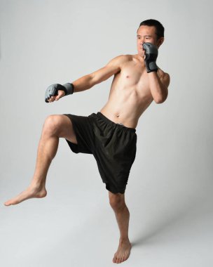 Formda, Asyalı bir erkek modelin tam boy portresi, kaslı üstsüz. Spor stenografisi boks eldiveni takıyor, hareketli yumruk pozu veriyor. Beyaz bir stüdyoda izole edilmiş..