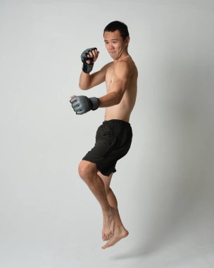 Formda, Asyalı bir erkek modelin tam boy portresi, kaslı üstsüz. Spor stenografisi boks eldiveni takıyor, hareketli yumruk pozu veriyor. Beyaz bir stüdyoda izole edilmiş..