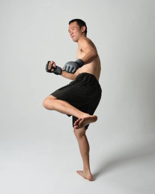 Formda, Asyalı bir erkek modelin tam boy portresi, kaslı üstsüz. Spor stenografisi boks eldiveni takıyor, hareketli yumruk pozu veriyor. Beyaz bir stüdyoda izole edilmiş..