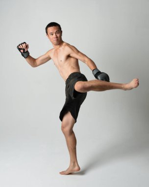 Formda, Asyalı bir erkek modelin tam boy portresi, kaslı üstsüz. Spor stenografisi boks eldiveni takıyor, hareketli yumruk pozu veriyor. Beyaz bir stüdyoda izole edilmiş..