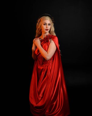 Kırmızı ipek toga elbisesi ve taç giyen, antik mitolojik fantezi tanrıçası gibi giyinmiş güzel sarışın mankenin yakın portresi. Karanlık stüdyo arka planında izole zarif bir poz..