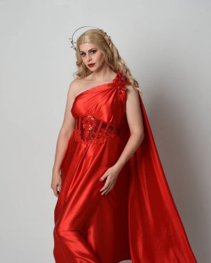 Kırmızı ipek toga elbisesi ve taç giyen, antik mitolojik fantezi tanrıçası gibi giyinmiş güzel sarışın mankenin yakın portresi. Stüdyoda izole edilmiş zarif bir poz..