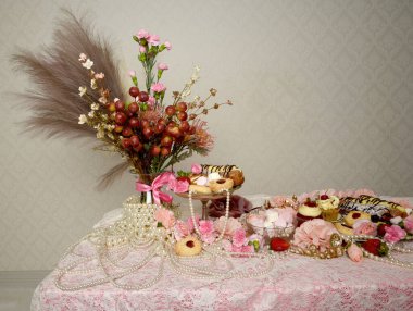 Pasta, pasta ve pembe lolipoplardan oluşan hoş bir ziyafetin portrelerini yakın plan zengin mücevherler, taçlar ve çiçekler arka planda güzel barok duvar kağıtları olan bir masanın üzerinde..