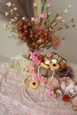 Pasta, pasta ve pembe lolipoplardan oluşan hoş bir ziyafetin portrelerini yakın plan zengin mücevherler, taçlar ve çiçekler arka planda güzel barok duvar kağıtları olan bir masanın üzerinde..