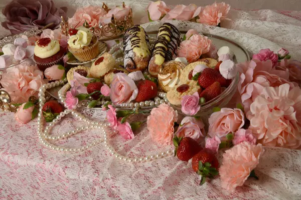Pasta, pasta ve pembe lolipoplardan oluşan hoş bir ziyafetin portrelerini yakın plan zengin mücevherler, taçlar ve çiçekler arka planda güzel barok duvar kağıtları olan bir masanın üzerinde..