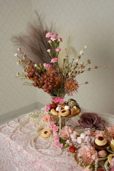 Pasta, pasta ve pembe lolipoplardan oluşan hoş bir ziyafetin portrelerini yakın plan zengin mücevherler, taçlar ve çiçekler arka planda güzel barok duvar kağıtları olan bir masanın üzerinde..