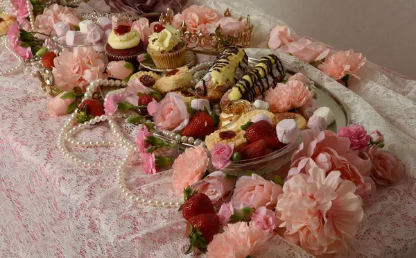 Pasta, pasta ve pembe lolipoplardan oluşan hoş bir ziyafetin portrelerini yakın plan zengin mücevherler, taçlar ve çiçekler arka planda güzel barok duvar kağıtları olan bir masanın üzerinde..