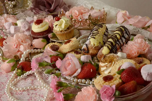 stock image close up portraits of an indulgent feast of cakes, pastries and pink lollies wit rich jewels and crowns and flowers on a table with pretty baroque wallpaper in background.