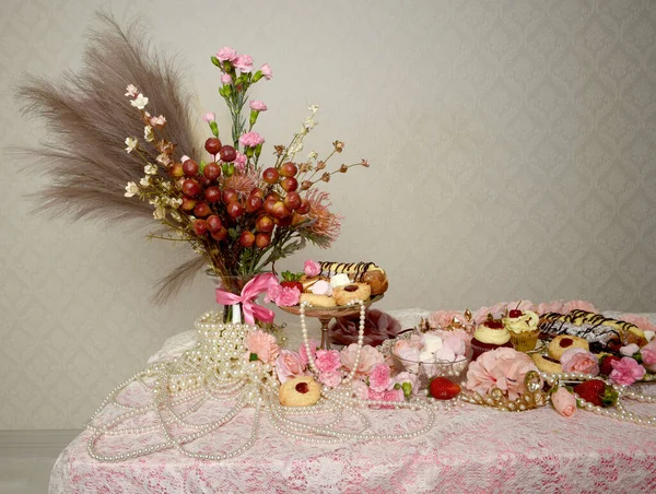 Pasta, pasta ve pembe lolipoplardan oluşan hoş bir ziyafetin portrelerini yakın plan zengin mücevherler, taçlar ve çiçekler arka planda güzel barok duvar kağıtları olan bir masanın üzerinde..