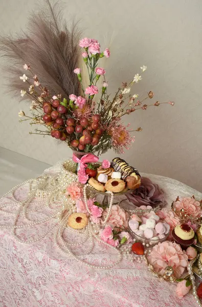 Pasta, pasta ve pembe lolipoplardan oluşan hoş bir ziyafetin portrelerini yakın plan zengin mücevherler, taçlar ve çiçekler arka planda güzel barok duvar kağıtları olan bir masanın üzerinde..