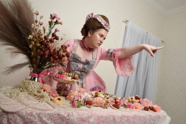 Zengin pembe bir elbise giyen sevimli bir kadın modelin portresi. Tarihi bir Fransız barok asilzadesinin kostümü. Pastalarla, çiçeklerle ve mücevherlerle ziyafet çekiyorlar.